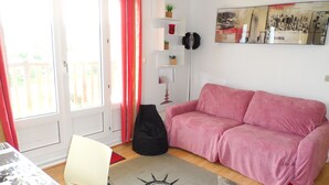 Un salón con un sofá rosa, un bolso negro, un tapete con estampado de estatua y una pintura de un paisaje urbano.
