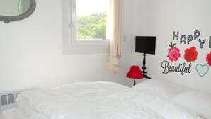 Un dormitorio con una cama, un televisor de pared, una lámpara roja y un ventanal con cortinas.