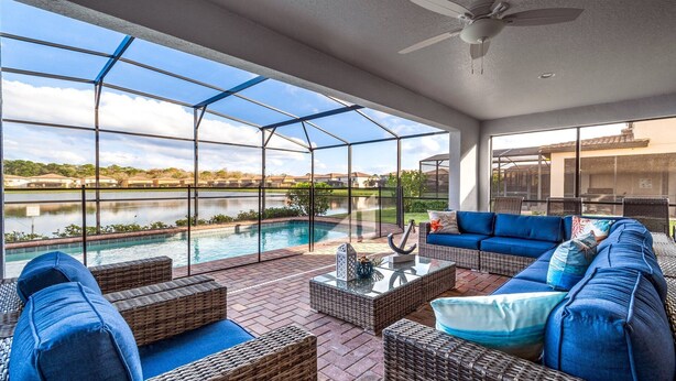 A covered outdoor area with a pool, wicker furniture, and a view of a lake. - Lakeview ~ Pool Moana Themed Escape w Game Room (Kissimmee)
