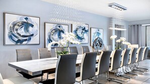 A modern dining area with a long table, multiple chairs, and abstract art on the walls. - Lakeview ~ Pool Moana Themed Escape w Game Room (Kissimmee)