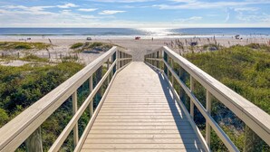 A wooden boardwalk leading to a beach with a clear view of the ocean and distant beachgoers. - Family Beach Condo - Steps To The Sand Or Pool (St. Augustine)