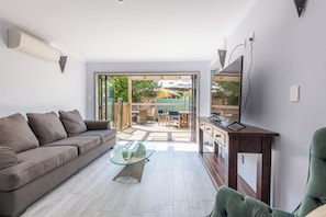 A modern living room with a sofa, a glass coffee table, and a TV on a wooden stand.