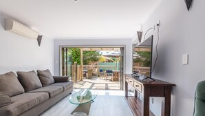 Un salon moderne avec un canapé, une table basse en verre et un téléviseur posé sur un meuble en bois.