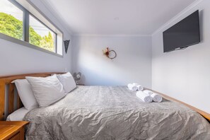 A bedroom with a bed, pillows, a wall-mounted TV, and a window with a view of trees.