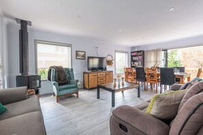A modern living room with a fireplace, a television, a dining area with chairs and a table, and a bookshelf.