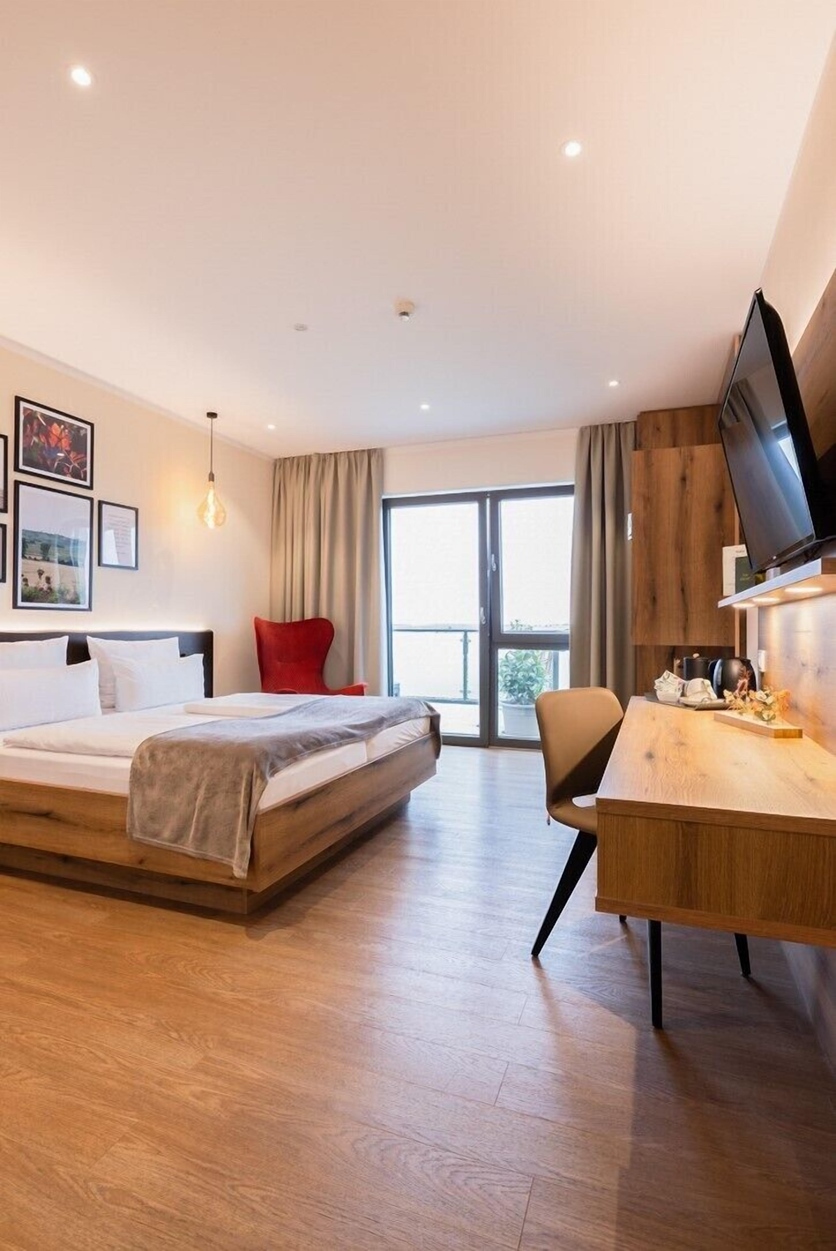 Una habitación de hotel moderna con una cama, un escritorio, un televisor y una silla roja.
