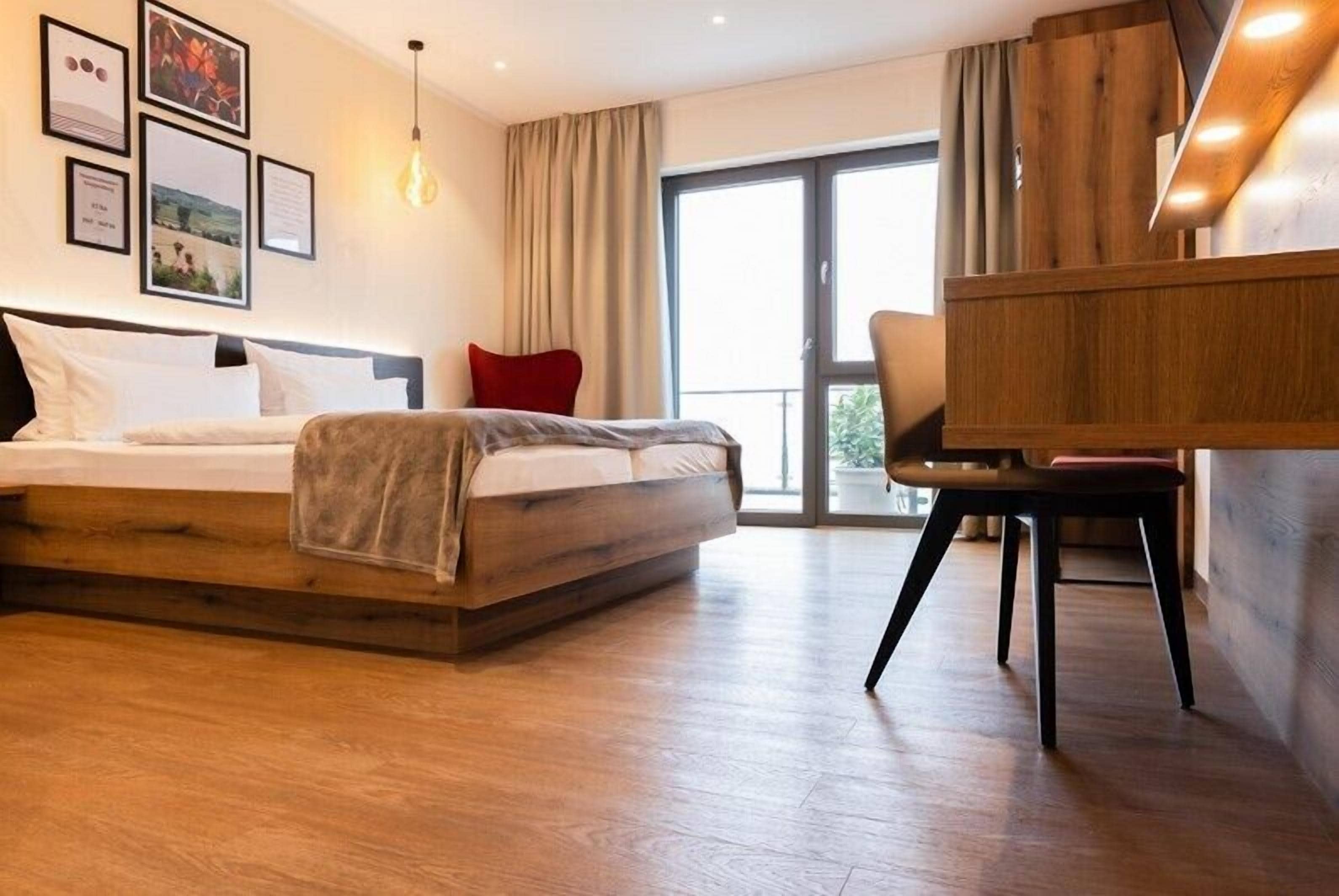 Habitació d'hotel moderna amb un llit gran, un escriptori de fusta i una finestra ampla que ofereix vistes a l'exterior.