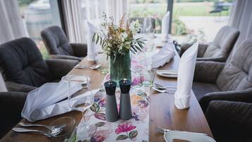 A dining table set with a floral tablecloth, two salt and pepper shakers, and a vase with flowers.