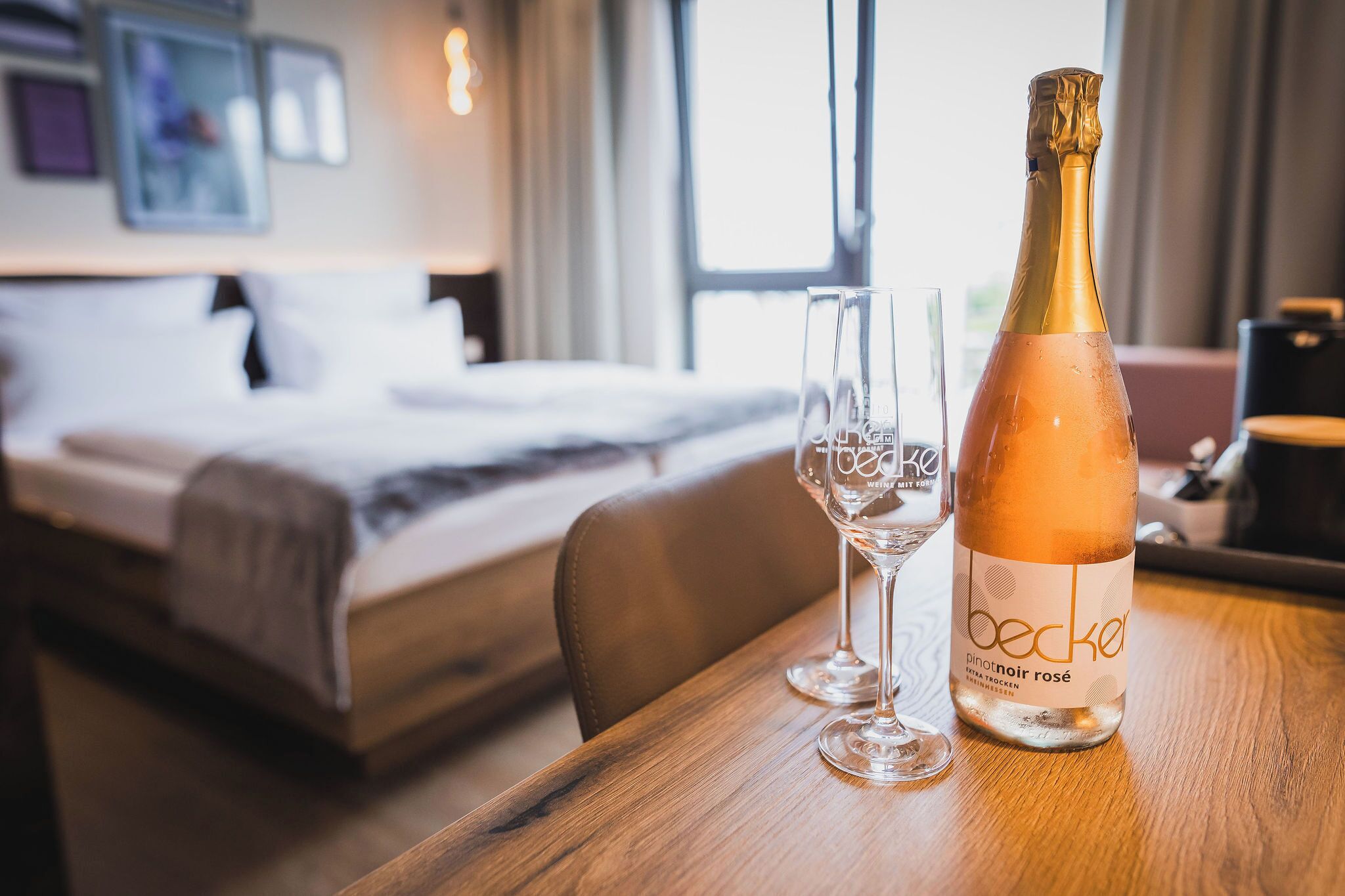 Une bouteille de Becker Pinot Noir Rosé sur une table en bois, avec deux verres à vin vides.
