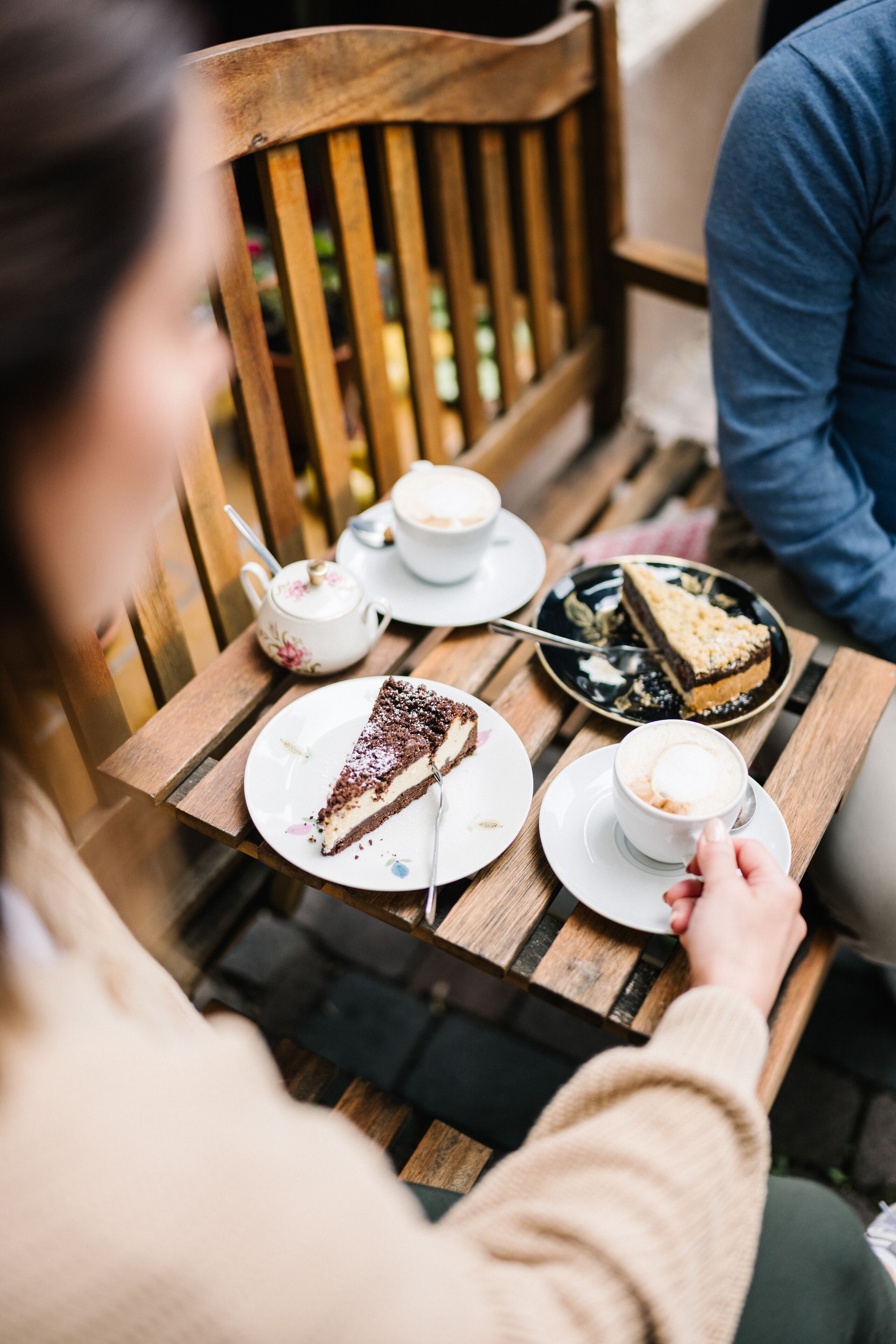 Ein Holztisch mit Kuchenstück, einer Kaffeetasse und einem Teekännchen.