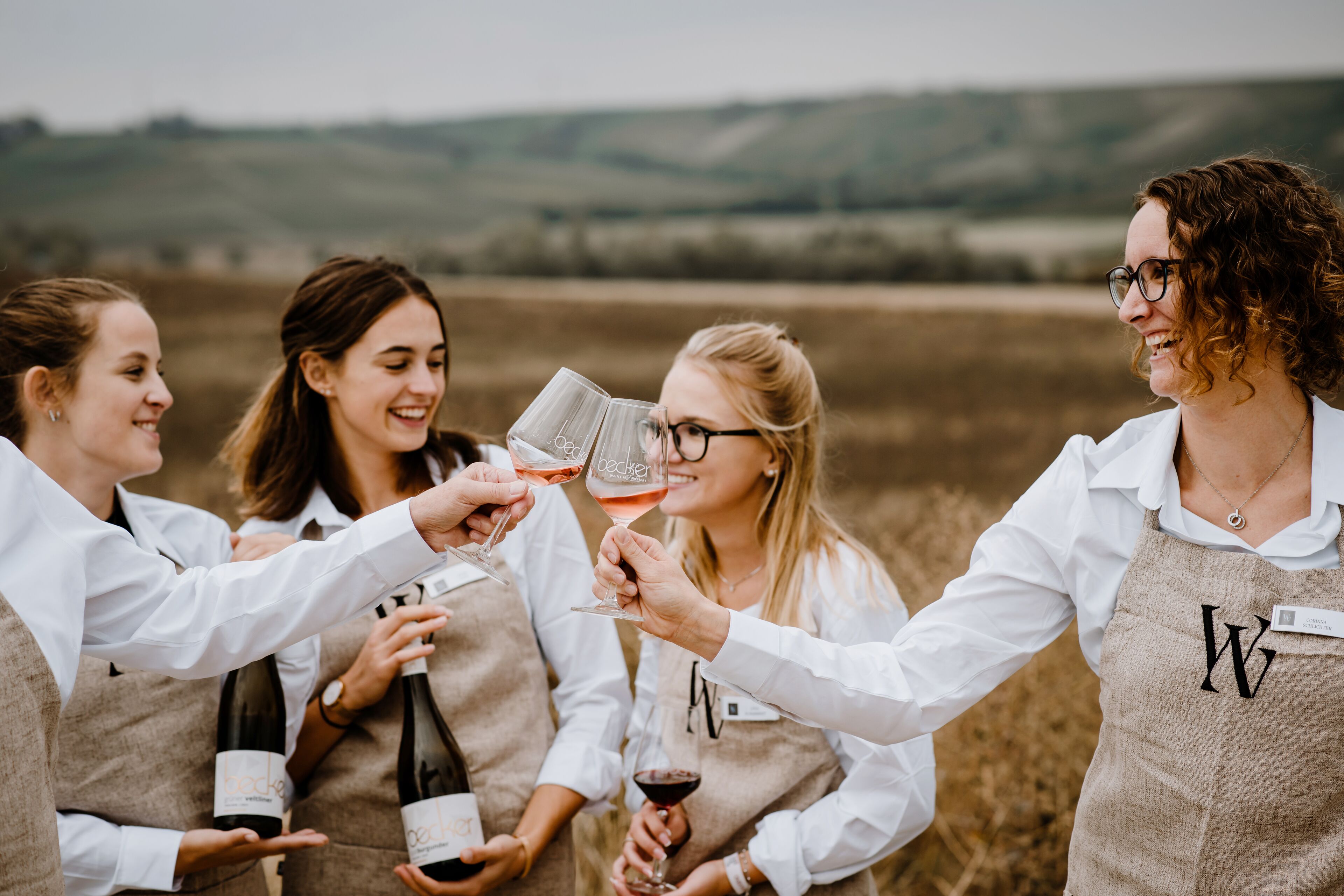 A group of people toasting with wine glasses in a vineyard setting.