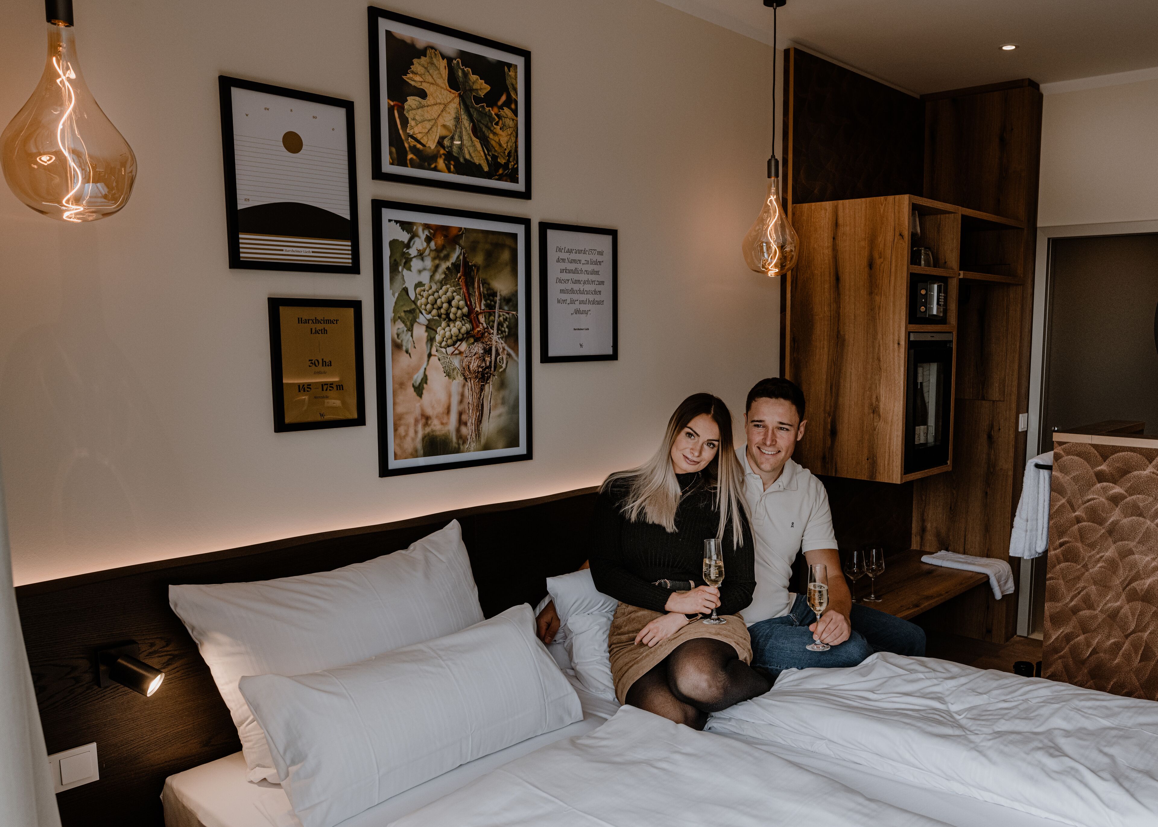 A hotel room with a bed, a wooden headboard, a wall-mounted shelf, and framed pictures.