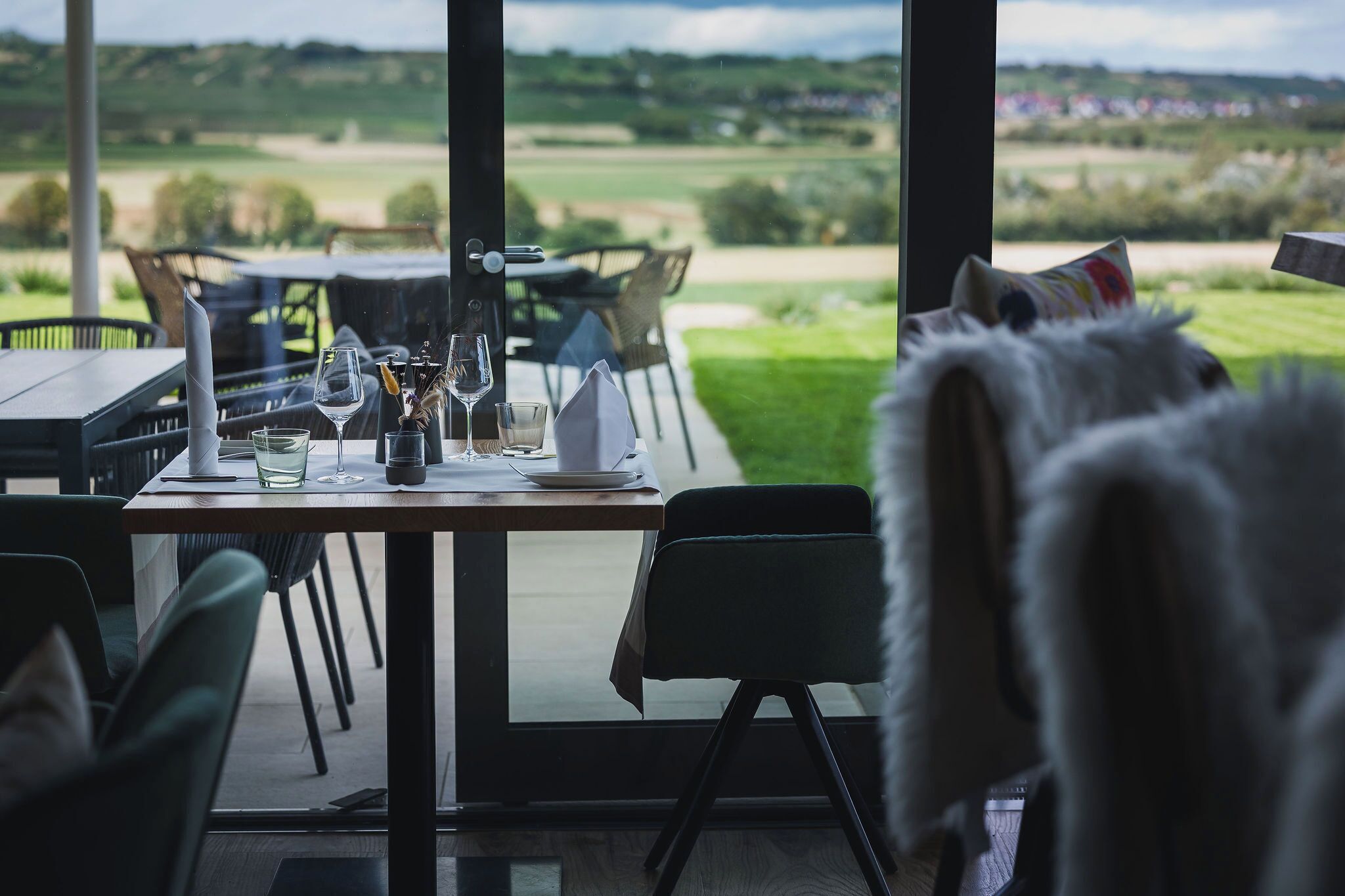 Un comedor con una mesa dispuesta para dos, vistas a un campo de golf y una butaca cubierta de piel blanca.