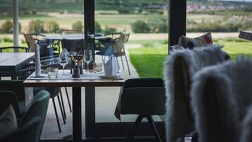 Un comedor con una mesa dispuesta para dos, vistas a un campo de golf y una butaca cubierta de piel blanca.