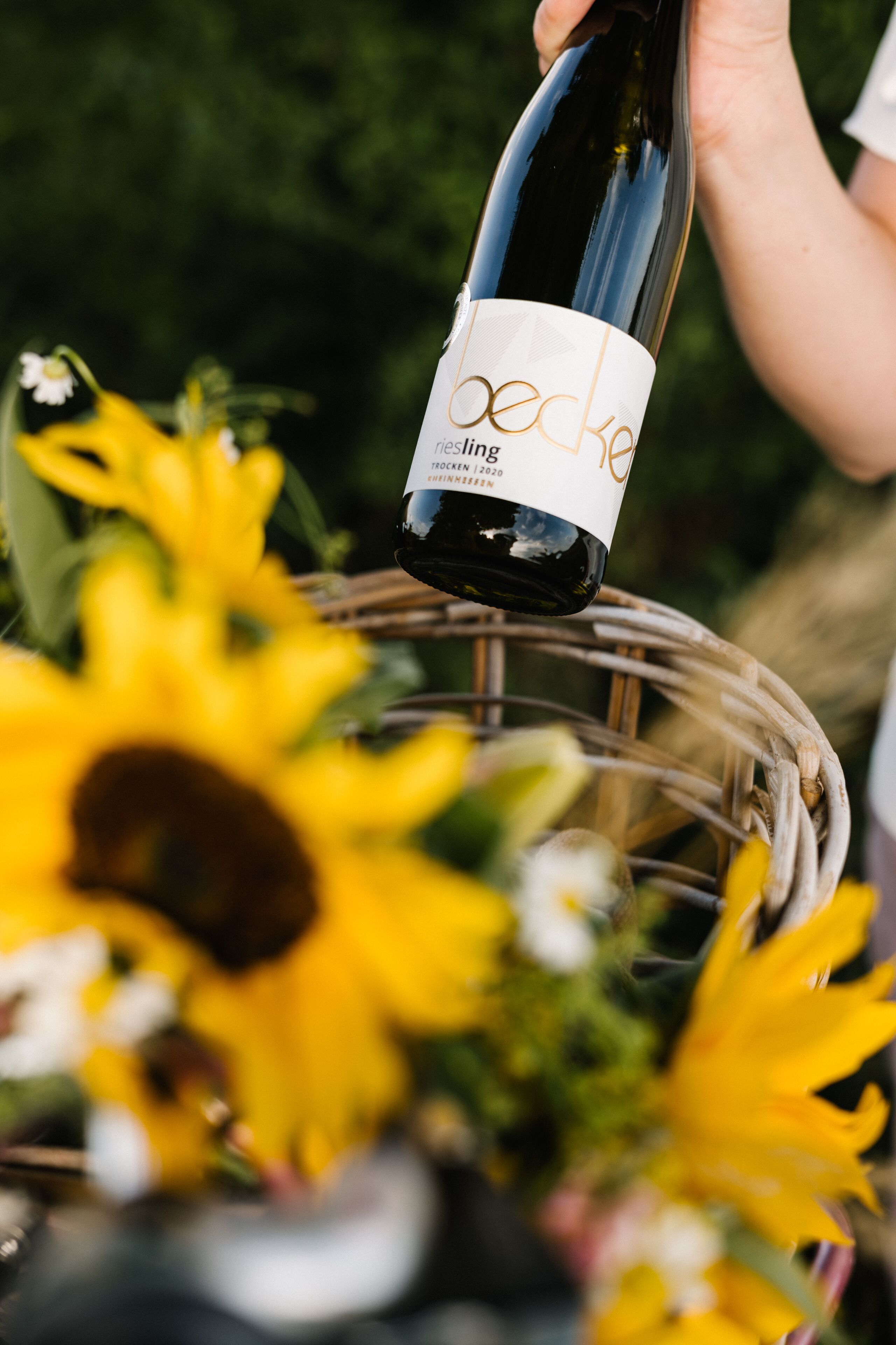 Una botella de vino Becke con etiqueta, sobre un atril de mimbre con girasoles.