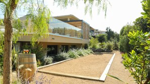 Ein modernes Haus mit einem Glasbalkon, einem Holzfass und einem Garten mit verschiedenen Pflanzen.