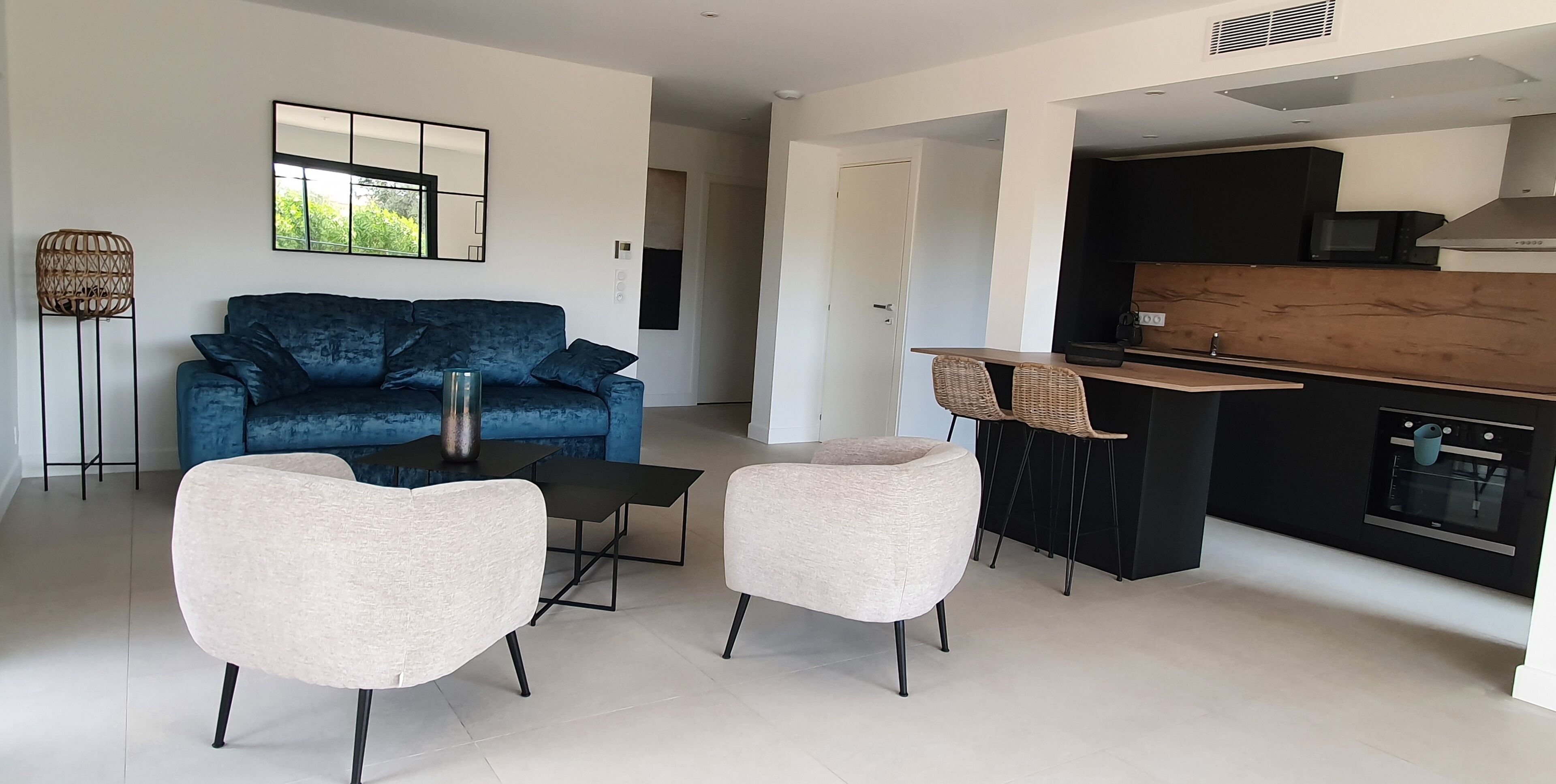 A modern living room with a blue sofa, two armchairs, a coffee table, and a kitchen area with a black countertop and white cabinets.