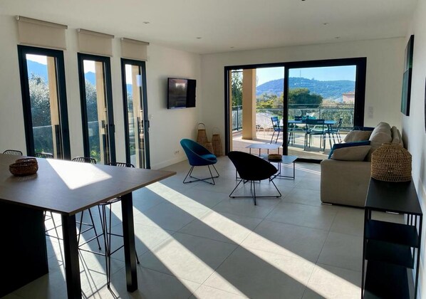 Uma sala de estar espaçosa com uma mesa de jantar, duas cadeiras, um sofá e uma varanda com vista para o exterior.