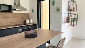 Eine moderne Küche mit Holzarbeitsplatte, schwarzen Schränken und einer schwarzen Netzkübel. Zwei Korbstühle und ein schwarzes Metallregal sind an der Wand angebracht.
