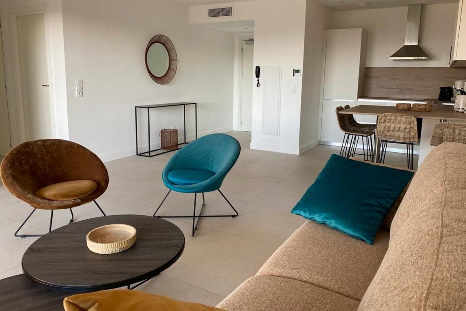 Una sala moderna con un sofá, dos sillones, una mesita de centro y una cocina al fondo.