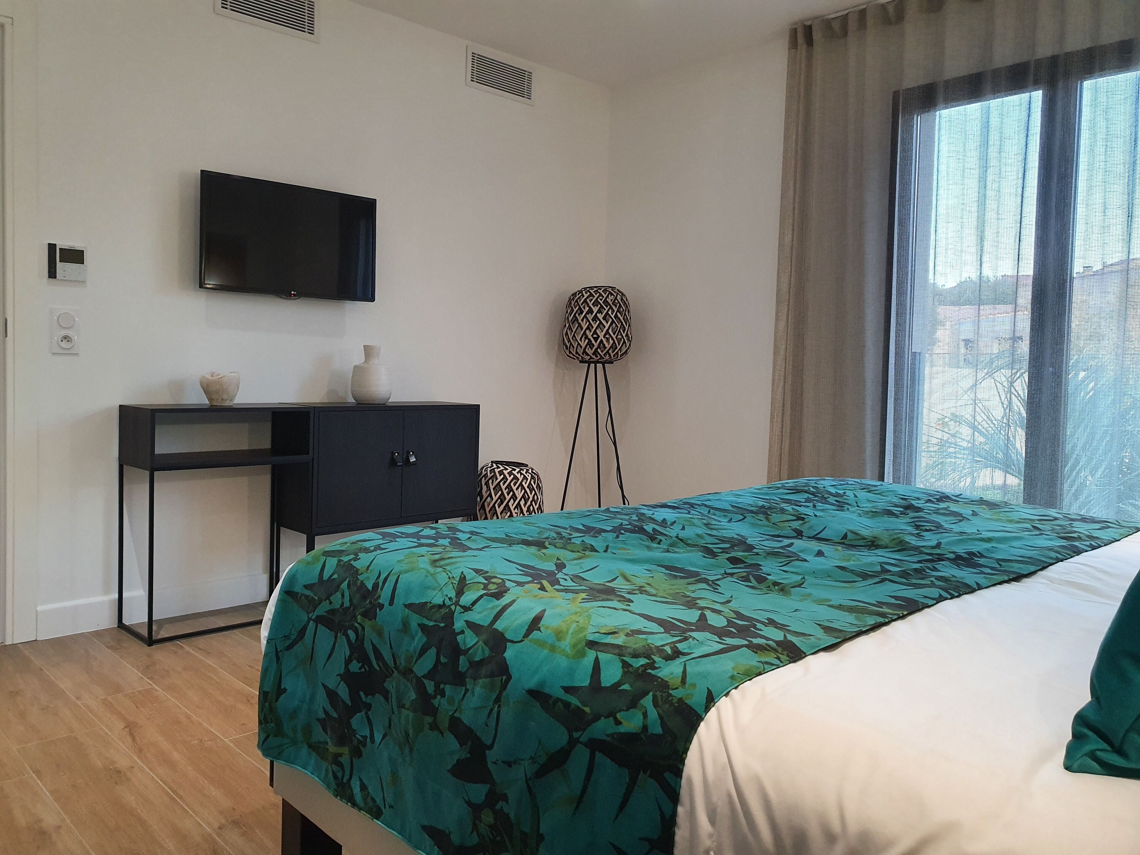 Un dormitorio con cama, escritorio, televisor y ventana con cortinas.