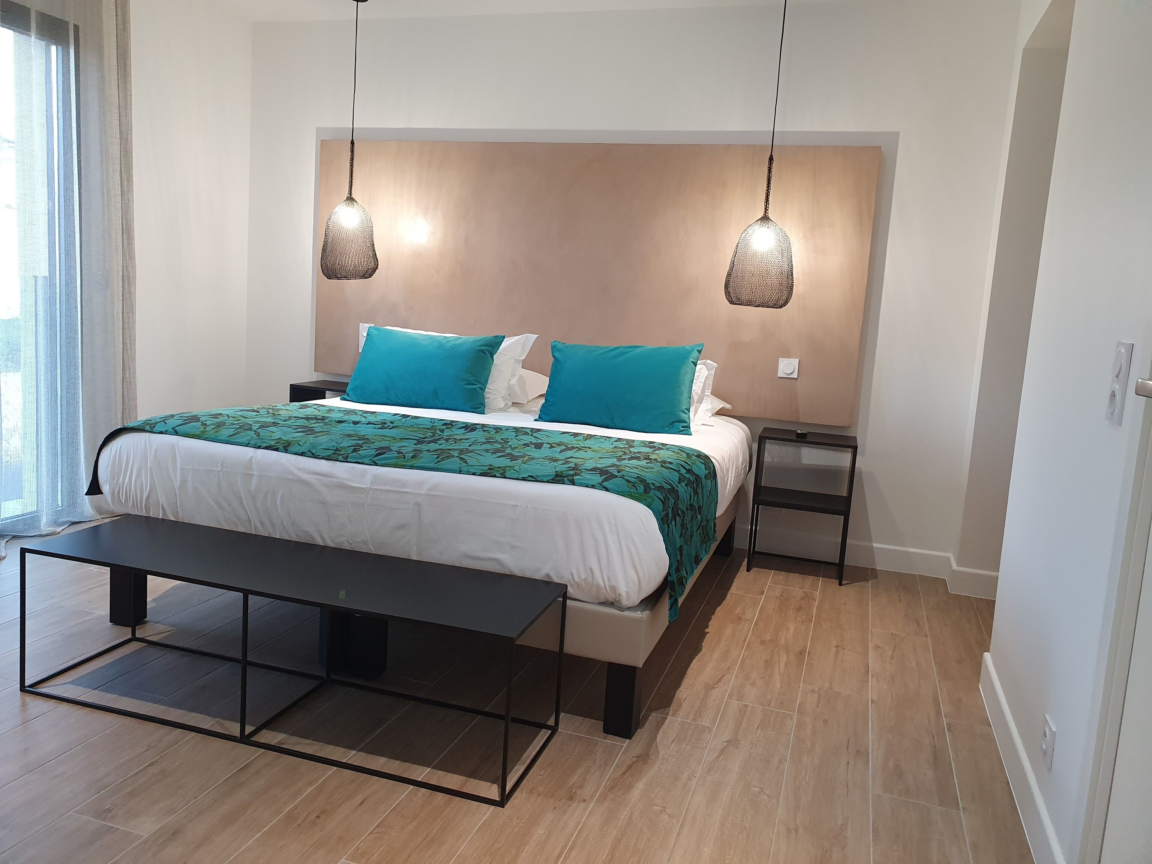 Ein modernes Schlafzimmer mit einem großen Bett, zwei Nachttischen, einer Bank und Pendelleuchten.