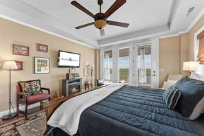 A bedroom with a large bed, a ceiling fan, a fireplace, and a television on the wall.