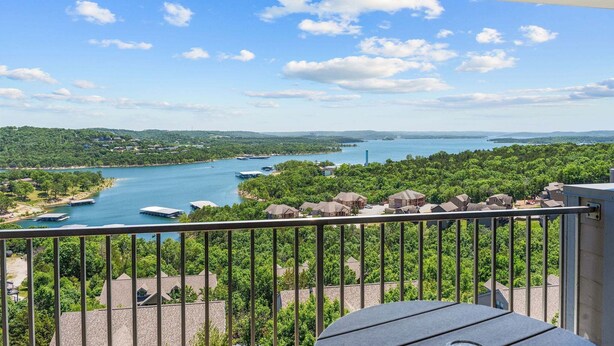 A balcony with a view of a lake, surrounded by greenery and buildings. - Lake View Retreat Near SDC with Free Tickets, Community Outdoor Pool & Upgraded Kitchen (Branson)