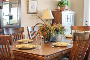 A dining table set for six with a centerpiece of flowers and foliage, surrounded by wooden chairs.