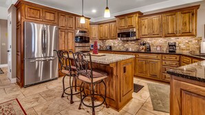A modern kitchen with wooden cabinets, stainless steel appliances, and a central island with bar stools. - Lake View Retreat Near SDC with Free Tickets, Community Outdoor Pool & Upgraded Kitchen (Branson)
