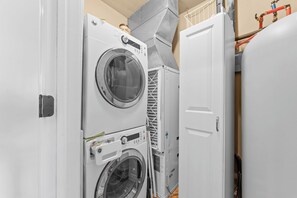 A laundry room with stacked washing machines and dryers, a metal vent, and a white door.