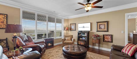 A living room with leather sofas, a fireplace, a ceiling fan, and a television.