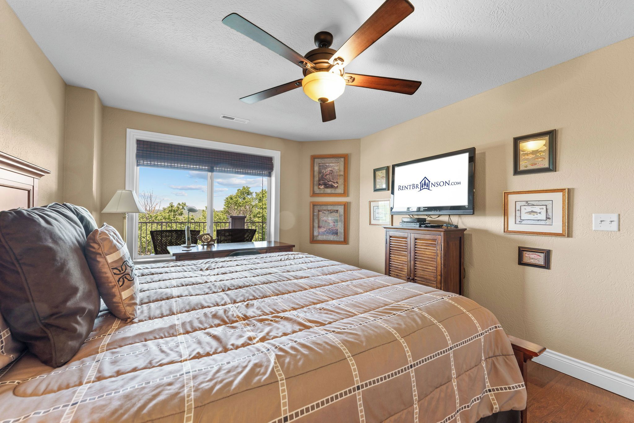 A bedroom with a bed, a ceiling fan, a TV, and framed pictures on the wall.