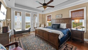 A bedroom with a bed, a ceiling fan, a nightstand, a bench, and a view of the outdoors. - Lake View Retreat Near SDC with Free Tickets, Community Outdoor Pool & Upgraded Kitchen (Branson)