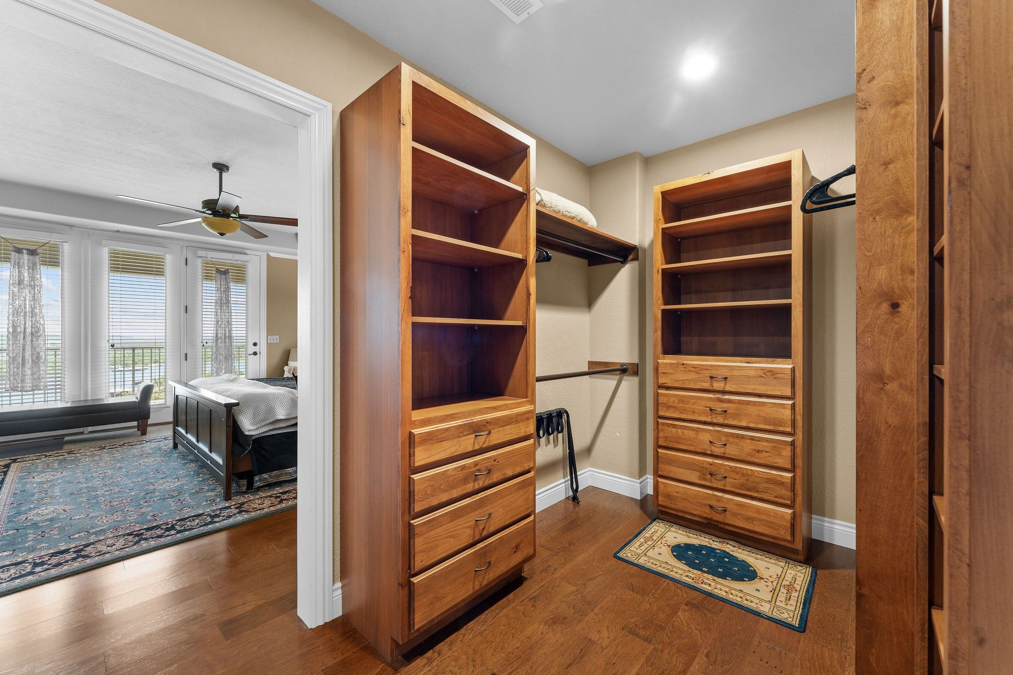 A room with a large wooden closet, a bed with a headboard, a ceiling fan, and a view of the outside through a window with blinds.