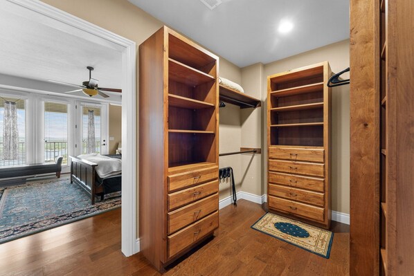 A room with a large wooden closet, a bed with a headboard, a ceiling fan, and a view of the outside through a window with blinds.