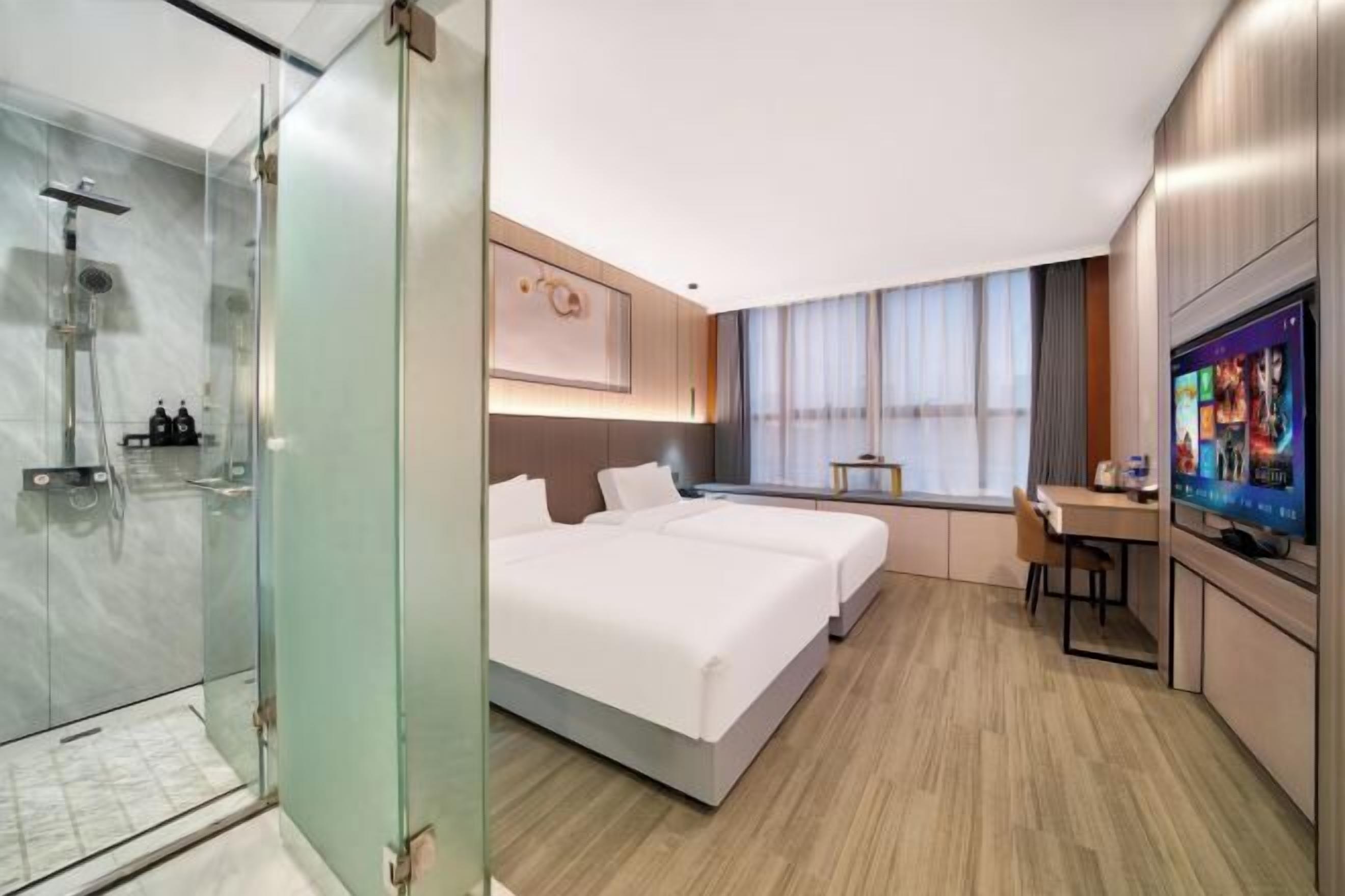 Une chambre d’hôtel moderne dotée d’une douche en verre, d’un grand lit avec deux oreillers, d’un bureau avec une chaise et d’un téléviseur fixé au mur.
