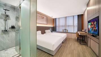 Une chambre d’hôtel moderne dotée d’une douche en verre, d’un grand lit avec deux oreillers, d’un bureau avec une chaise et d’un téléviseur fixé au mur.