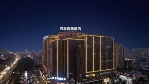 A multi-story hotel with illuminated vertical lines on the facade, a parking lot in front, and a clear view of the surrounding urban area at night. - Four Seasons Qingteng Hotel (Outlet Airport) (Ningbo)