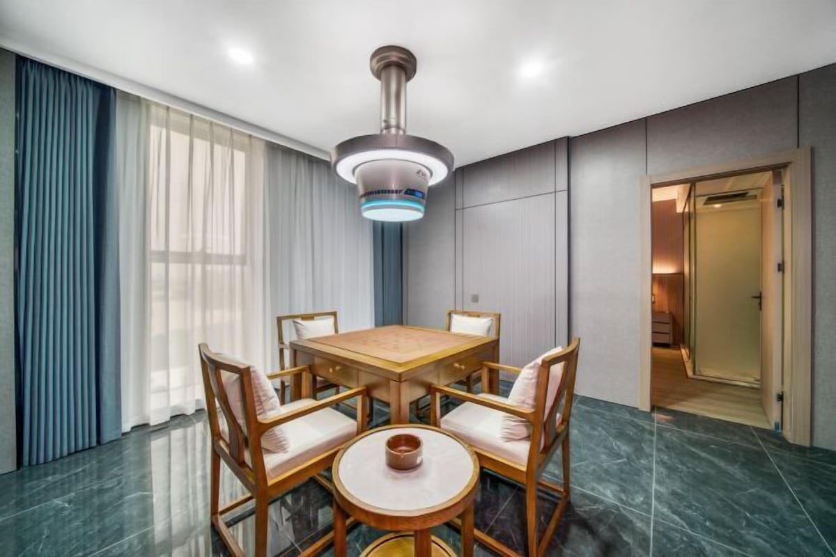 A dining area with a wooden table and chairs, a modern pendant light, and a view of a hallway.