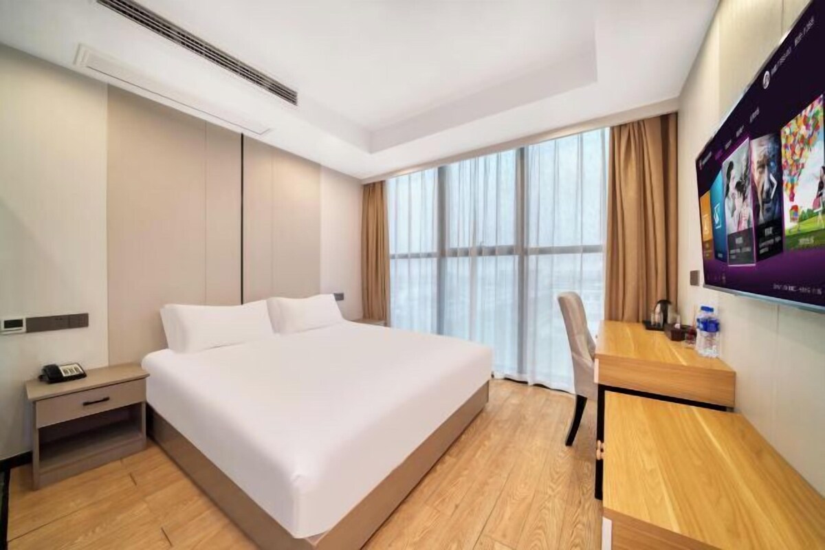 A hotel room with a large bed, a desk, a chair, a TV, and a window with curtains.