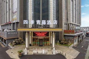 A hotel entrance with a large digital sign, a stone facade, and a small garden area with statues. - Four Seasons Qingteng Hotel (Outlet Airport) (Ningbo)