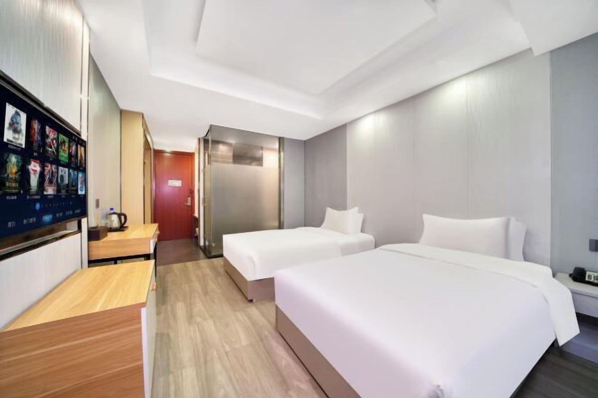 A hotel room with two beds, a wooden desk, a TV, and a red door.