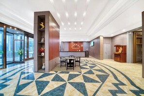 A hotel lobby with a reception desk, a seating area, and a patterned floor. - Four Seasons Qingteng Hotel (Outlet Airport) (Ningbo)