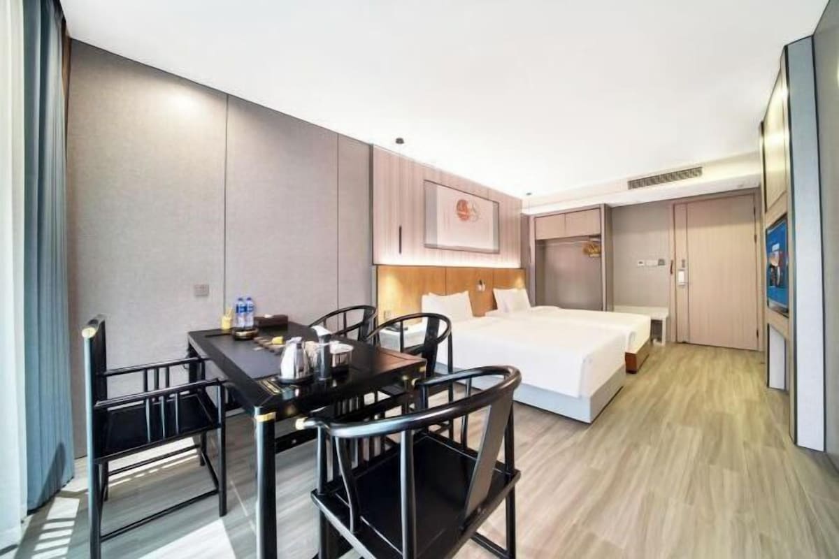 A hotel room with a bed, a desk with chairs, a small table, and a wall-mounted TV.