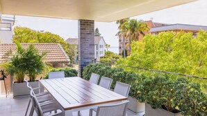 A balcony with a wooden table and chairs, surrounded by lush greenery and overlooking a residential area. - 5 Kingfisher, 5-7 Ondine Close, Nelson Bay, luxury apartment with Wifi and air conditioning (Nelson Bay)