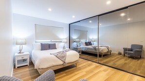 A modern bedroom with a large mirror, a bed with a headboard, bedside tables with lamps, and a chair. - 5 Kingfisher, 5-7 Ondine Close, Nelson Bay, luxury apartment with Wifi and air conditioning (Nelson Bay)