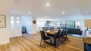 A modern kitchen with a central island, dining area with a wooden table and chairs, and a living area with a sofa and a large window. - 5 Kingfisher, 5-7 Ondine Close, Nelson Bay, luxury apartment with Wifi and air conditioning (Nelson Bay)