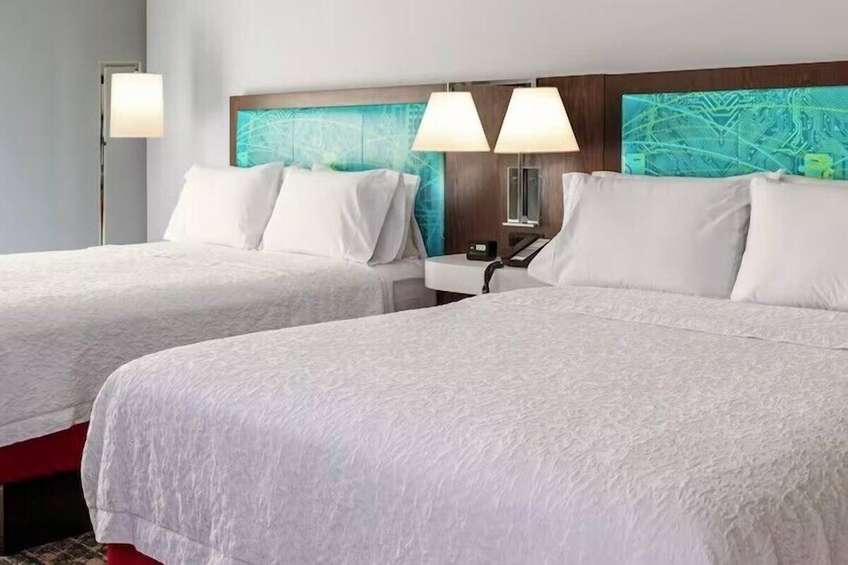 A hotel room with two beds, a nightstand with a lamp, and a wall with a map design.