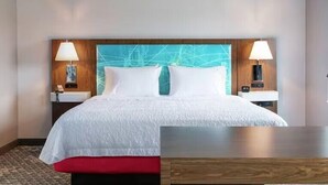 A hotel room with a large bed, two bedside tables with lamps, a wooden headboard with a geometric design, and a red bench at the foot of the bed. - Hampton Inn & Suites Chico (Chico)